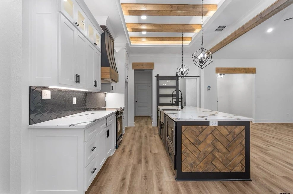 Custom kitchen interior with exposed wood beams, marble countertops, and herringbone island design by Prince Designs